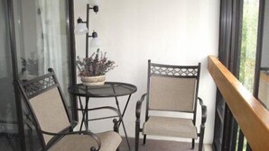 Ein kleiner Balkon mit zwei Stühlen, einem Tisch, einer Topfpflanze und einer Wandleuchte.