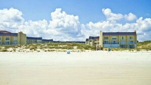 A beachfront hotel with multiple buildings, sandy beach, and dunes.