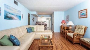 A living room with a sofa, coffee table, and chairs. There is a dining area with a table and chairs.