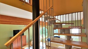 A multi-level wooden staircase with metal railings, a wooden desk, and a sofa in a living area with a view of greenery outside. - LaBarbe Bleu on Lake Michigan (Saint Ignace)