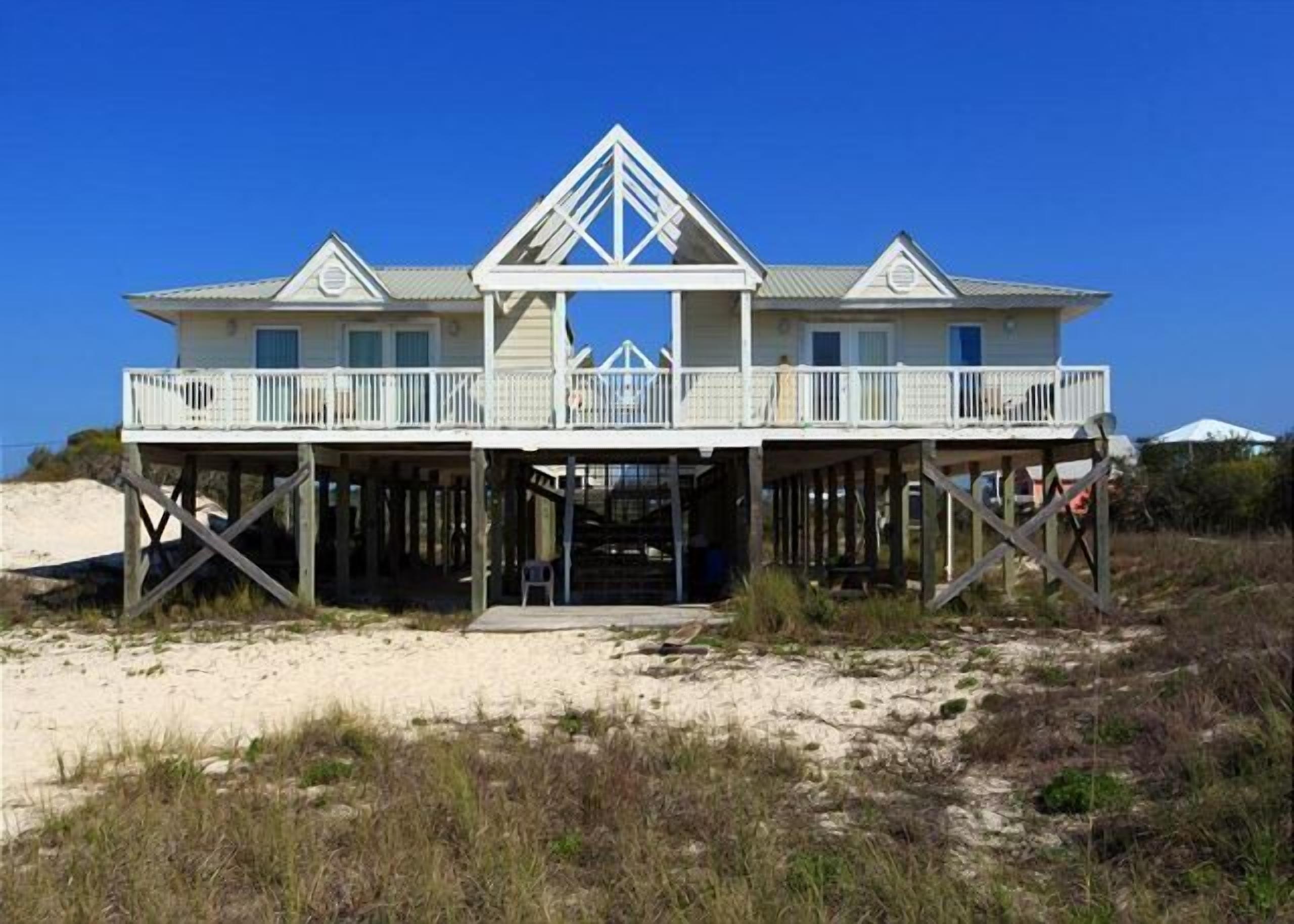 Une maison située en bord de mer, dotée d’un balcon, d’une terrasse en bois et offrant une vue dégagée sur la plage.