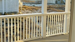 A beachfront property with a wooden deck, a beach view, and a two-story house with a balcony.