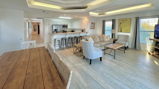 A spacious living area with a wooden dining table, a sofa, and a kitchen in the background.