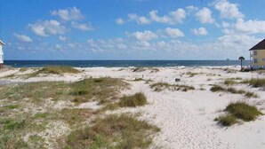 A beach with sand dunes, a clear sky, and a few buildings in the distance.