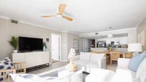A modern living room with a flat-screen TV, white sofas, a dining area, and a kitchen in the background. - Stay @ Paradise Peak on Folly Beach (Folly Beach)