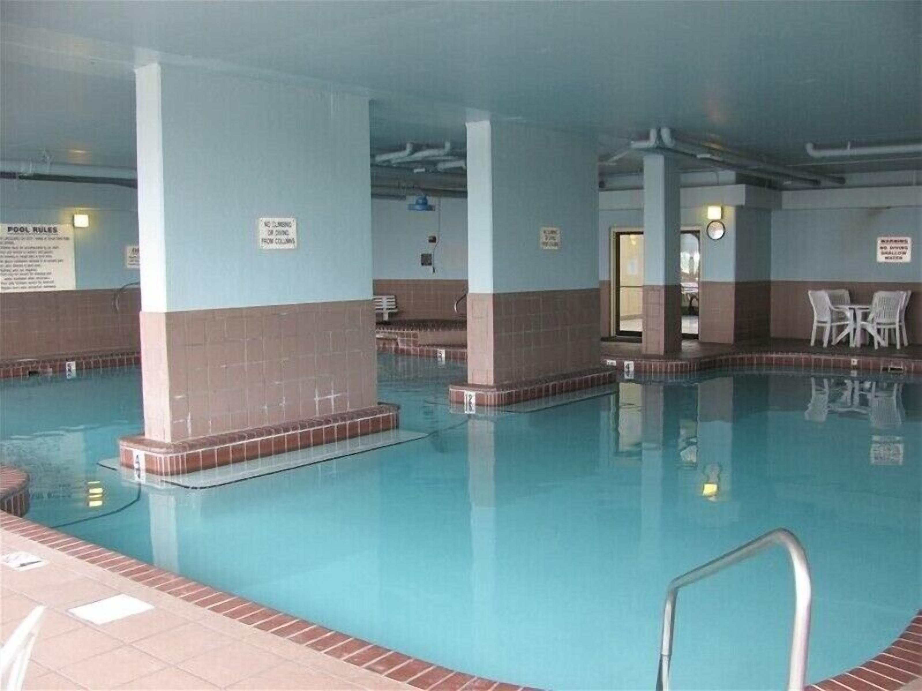 A swimming pool with tiled walls, a no climbing sign, and a clock on the wall.