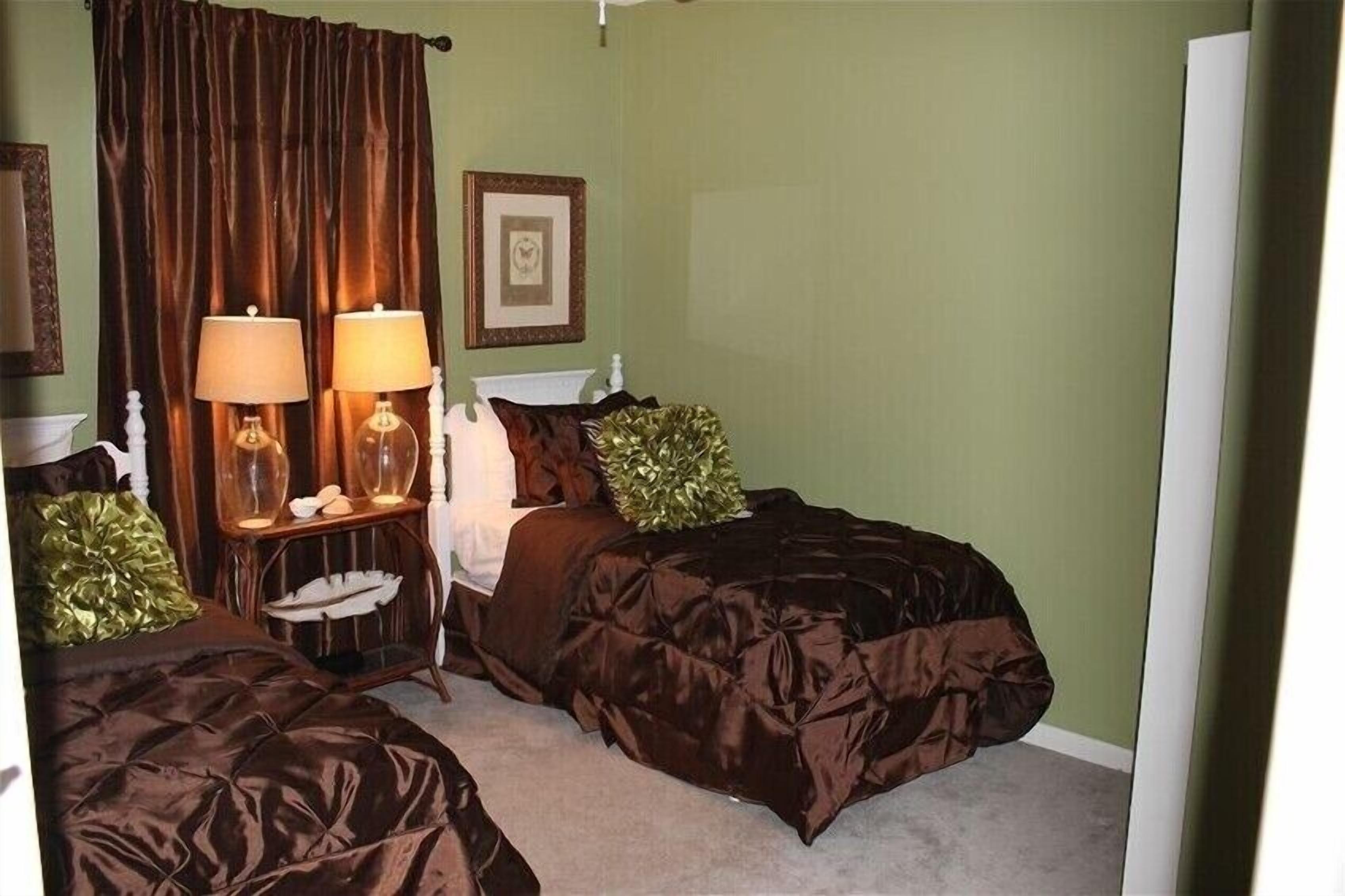 A bedroom with two beds, a nightstand with lamps, a framed picture on the wall, and a green wall.