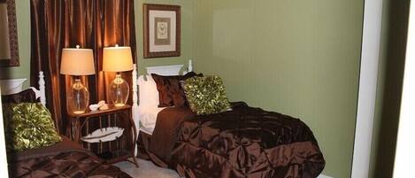 A bedroom with two beds, a nightstand with lamps, a framed picture on the wall, and a green wall.