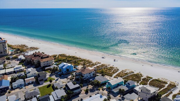 An aerial view of a coastal area with a beach, houses, and a clear blue sky.