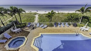 A rooftop pool with a view of the beach, lounge chairs, and a hot tub.