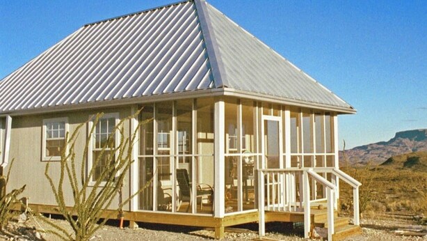 A single-story building with a metal roof, large windows, and a wooden deck. - Terlingua Ranch Retreat: Enviro Friendly Home (Terlingua)