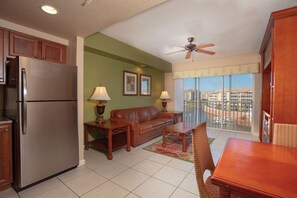 A compact living space with a kitchenette, a sofa, a dining table, and a balcony with a view of buildings.
