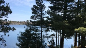 En stig som går längs sjön och leder fram till en brygga, omgiven av höga träd och en klar himmel.