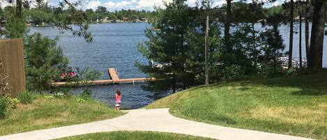 A grassy area with a concrete path leading to a dock by a lake.
