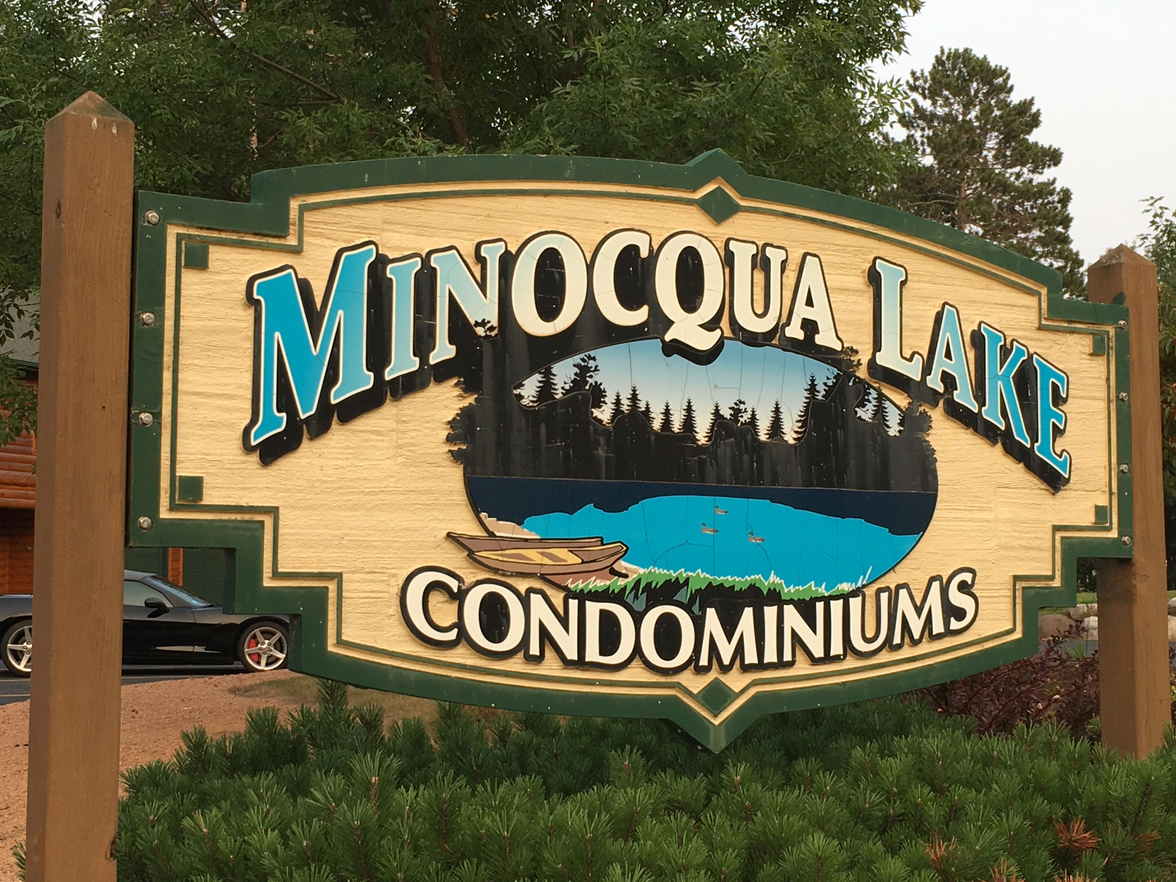 A sign for Minocqua Lake Condominiums with a lake and forest background.