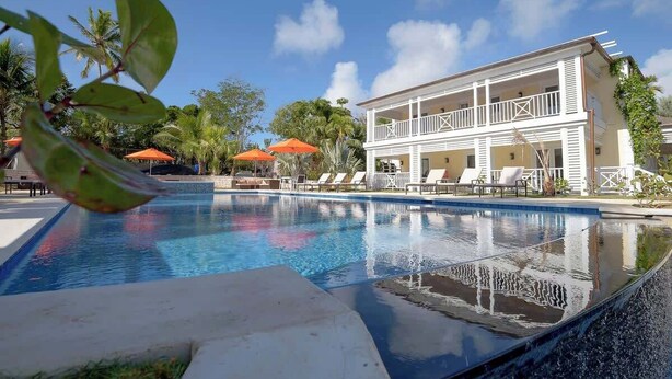 Une piscine avec un bâtiment blanc en arrière-plan, entourée de palmiers et de parasols orange.