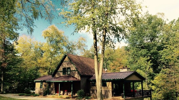 Une cabane rustique avec un toit en pente, entourée d’arbres et bordée d’une pelouse.