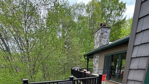 Une terrasse en bois avec des meubles d’extérieur, une cheminée en pierre et une porte vitrée donnant sur un espace intérieur.