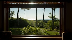 A window with a view of a lush green landscape and tall trees. - Magnificent Water View Condo (Egg Harbor)