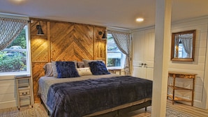 Ein Schlafzimmer mit einem großen Bett, einem Holzkopfende, Nachttischen, einem Spiegel und Blick auf Grün.