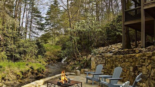Eine Terrasse im Freien mit Feuerstelle, Steinmauer und Adirondack-Stühlen.