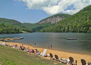 A lakeside scene at the Sapphire Valley Rec Center with a sandy beach, lounge chairs, and a dock.