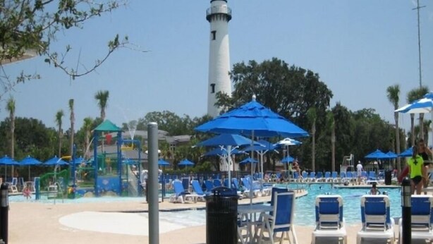 A pool area with lounge chairs, umbrellas, and a lighthouse in the background. - Located in desirable Ocean Walk, short walk to ocean and village (St Simons Island)