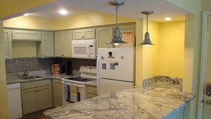 A compact kitchen with a granite countertop, white appliances, and yellow walls. - Located in desirable Ocean Walk, short walk to ocean and village (St Simons Island)