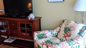 A living room with a wooden cabinet, a television, a floral sofa, and a round table with a dark surface. - Located in desirable Ocean Walk, short walk to ocean and village (St Simons Island)