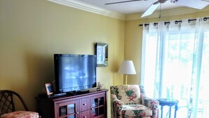 A living room with a television, a floral armchair, a coffee table, and a bar stool. - Located in desirable Ocean Walk, short walk to ocean and village (St Simons Island)