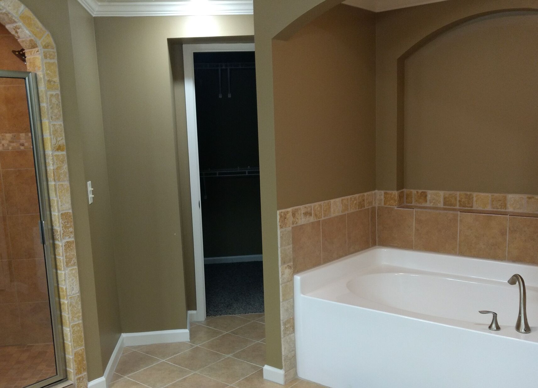 A bathroom with a bathtub, a shower area, and a door leading to another room.