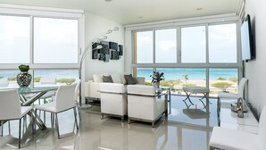 Una sala de estar moderna con un sofá blanco, una mesa de comedor de vidrio y vista a la playa.