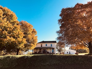 Uma casa de dois andares com varanda, rodeada por árvores com folhagem outonal.