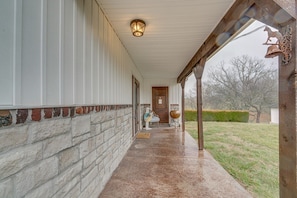 A covered porch with a stone wall, a wooden door, and a metal bell. - 4bd / 3ba Farmhouse Located Between Springfield and Branson, MO (Ozark)