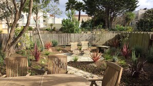 A patio area with a round wooden table and chairs, surrounded by a variety of plants and a wooden fence. - Spacious and Charming Marina District Home Steps from the Bay (SF)
