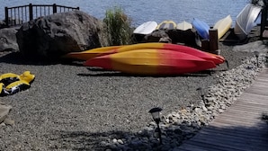 A lakeside view with a wooden dock, kayaks, and a rocky shoreline.