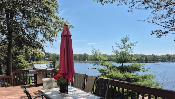 A deck with a table and chairs, a grill, and a view of a lake.