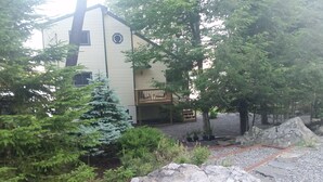 A two-story building with a balcony, surrounded by trees and a gravel path.