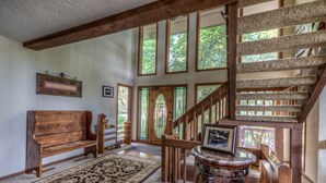 A spacious room with a wooden bench, a patterned rug, a small table with a picture, and a wooden staircase.