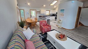 A living room with a sofa, a coffee table, and a dining area with chairs and a table. - Private Whalehead Beach Retreat - Pool, Hot Tub & 5-Minute Walk to the Ocean! (Corolla)