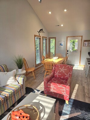 A living room with a sofa, a dining table with chairs, a red patterned chair, a potted plant, and a door with a window.