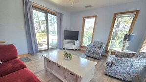 A living room with a red sofa, a white coffee table with plants, a TV, and patterned armchairs. - Private Whalehead Beach Retreat - Pool, Hot Tub & 5-Minute Walk to the Ocean! (Corolla)
