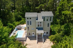 A two-story house with a swimming pool, surrounded by dense trees.