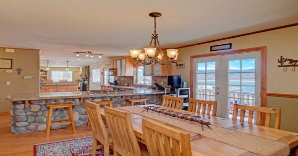 A spacious kitchen with a stone island, wooden dining table, and chairs. There is a large window with a view, a chandelier, and a television. - Lake Front, Rockies, Hiking, Mtn Biking! Aug. & Sept. Deals! (Monument)