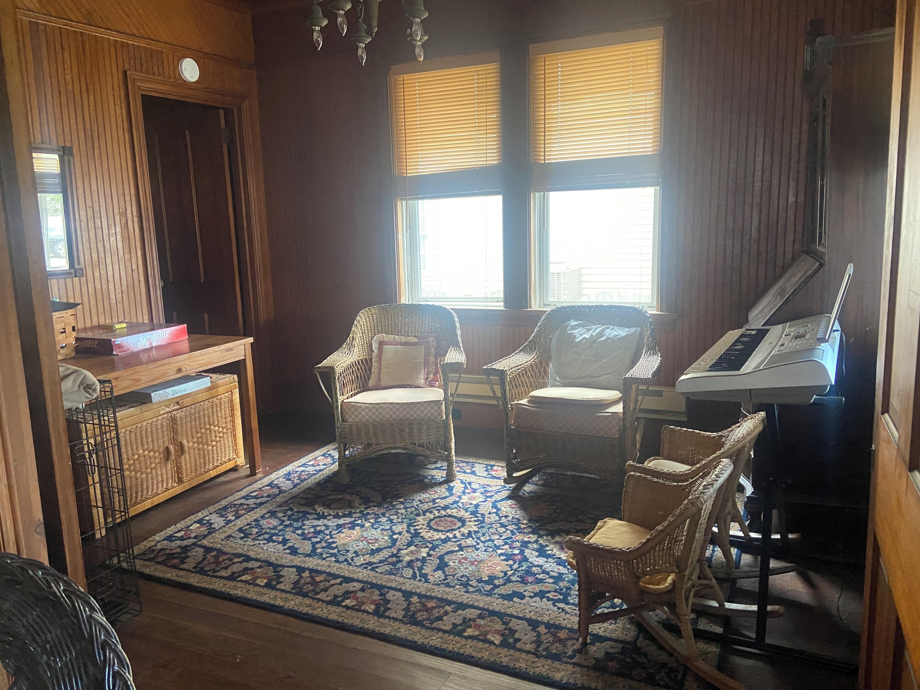 A cozy room with a piano, two wicker chairs, a wooden cabinet, and a patterned rug.
