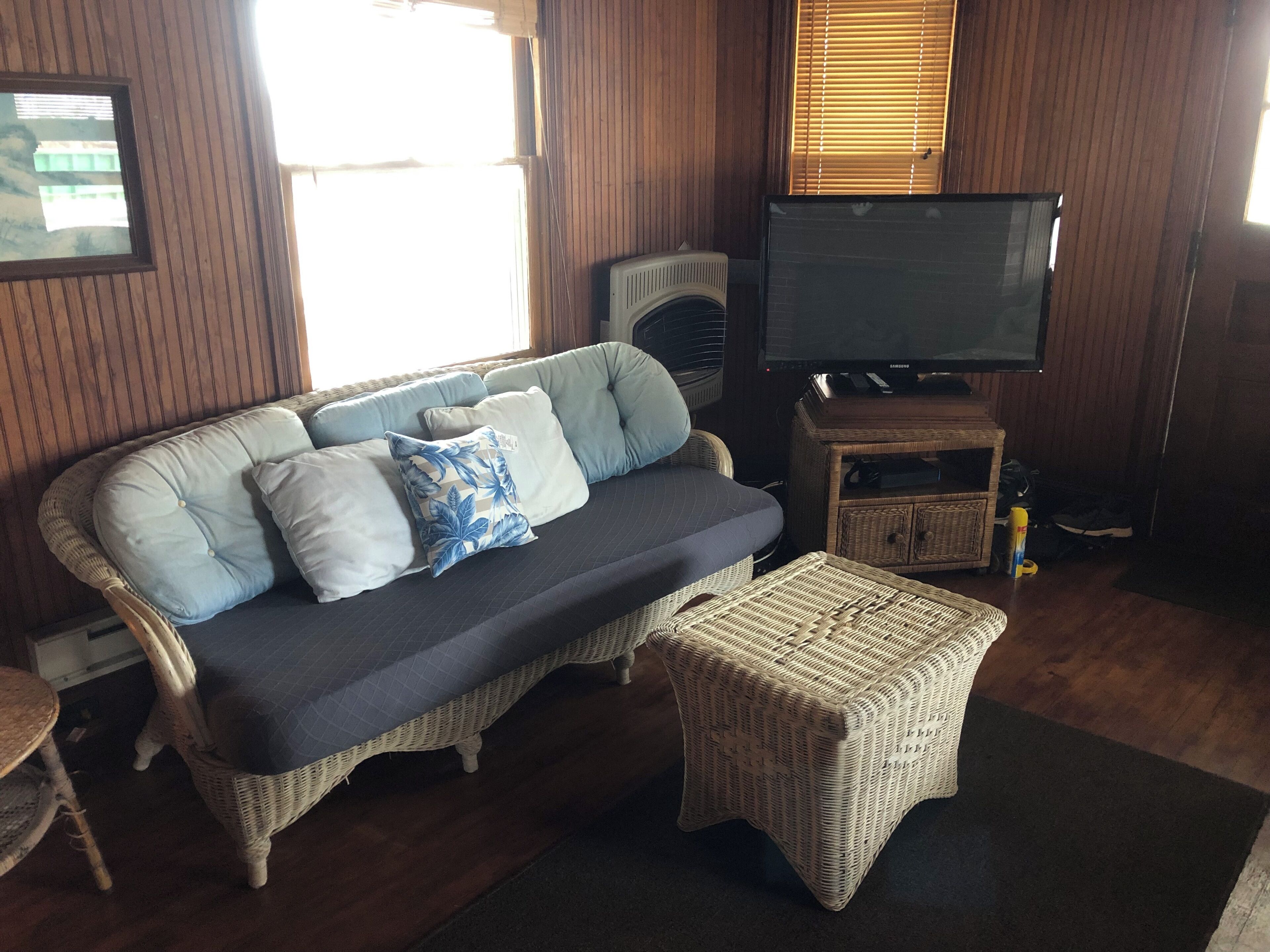 A living room with a sofa, ottoman, television, and wicker furniture.