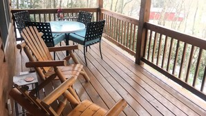 Een houten terras met een ronde tafel en stoelen, een leuning en uitzicht op bomen en gebouwen.