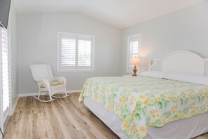 A bedroom with a bed, rocking chair, and two windows.