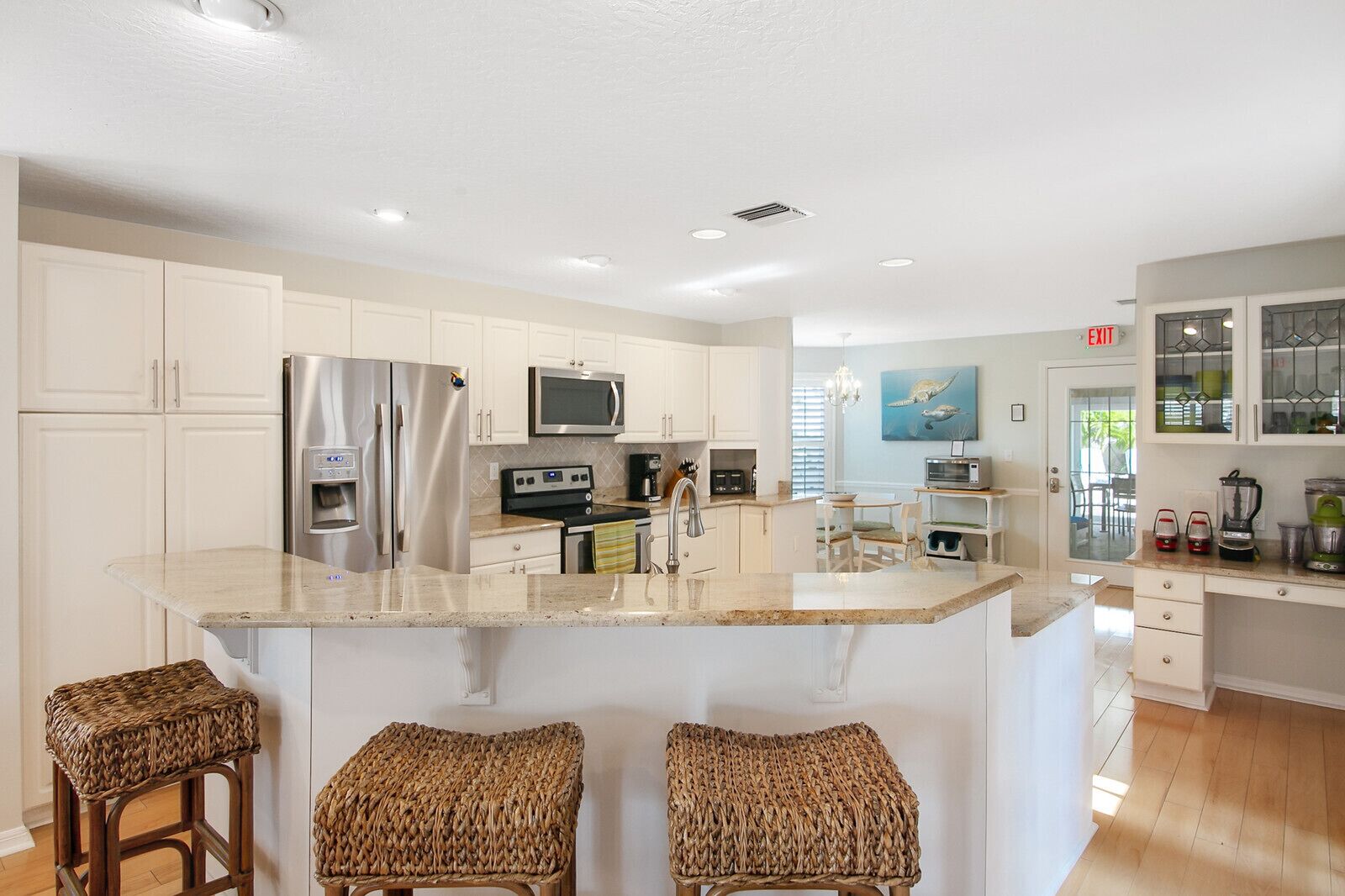 A modern kitchen with white cabinets, stainless steel appliances, a central island with bar stools, and a view to the dining area.