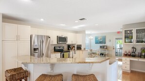 A modern kitchen with white cabinets, stainless steel appliances, a central island with bar stools, and a view to the dining area. - 5 BD, 3 bath, 200 Yards to Cocoa Beach (Cocoa Beach)